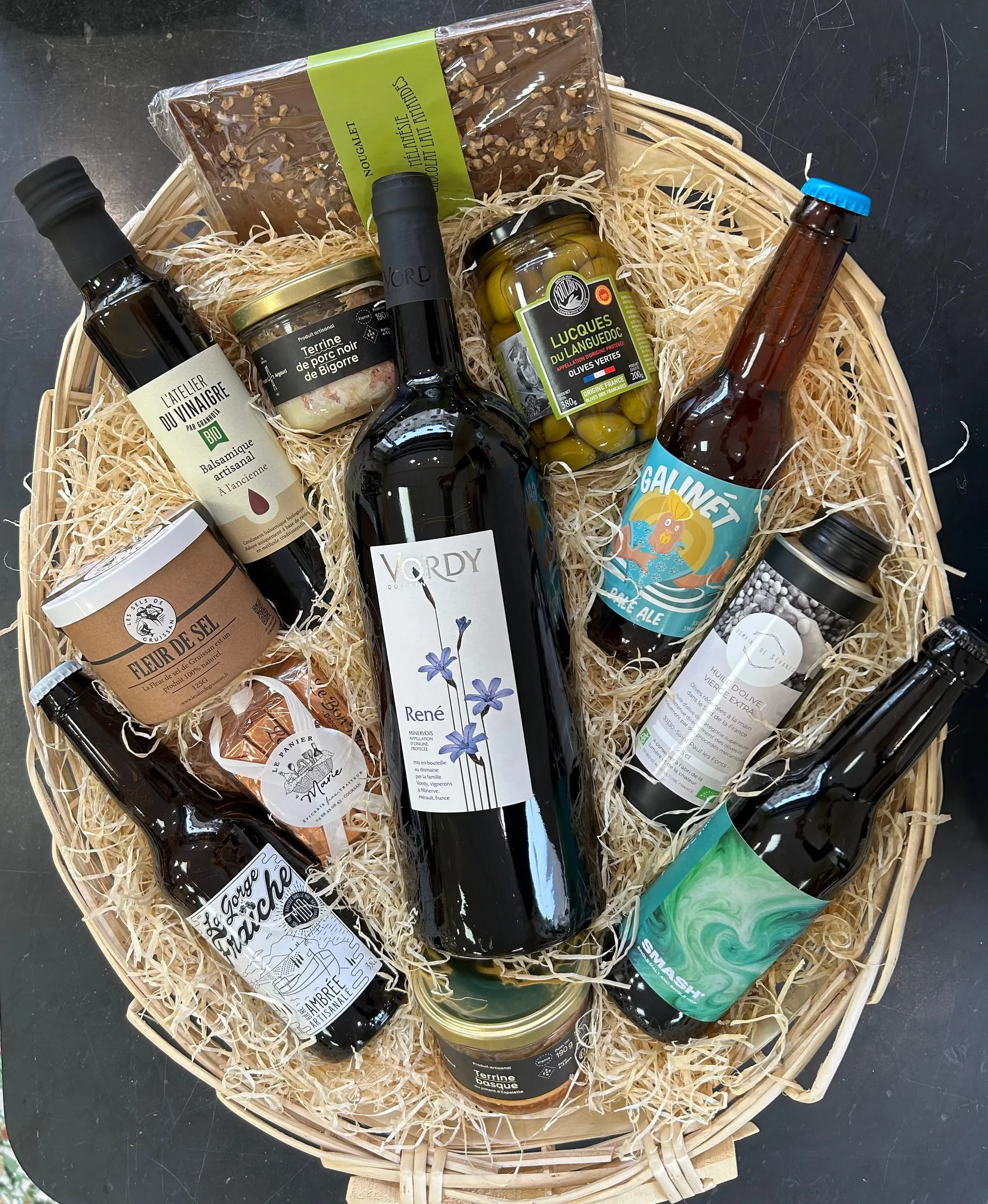 Panier gourmand garni de bouteilles de vin et de bière, d’huile, d’olives et de terrines