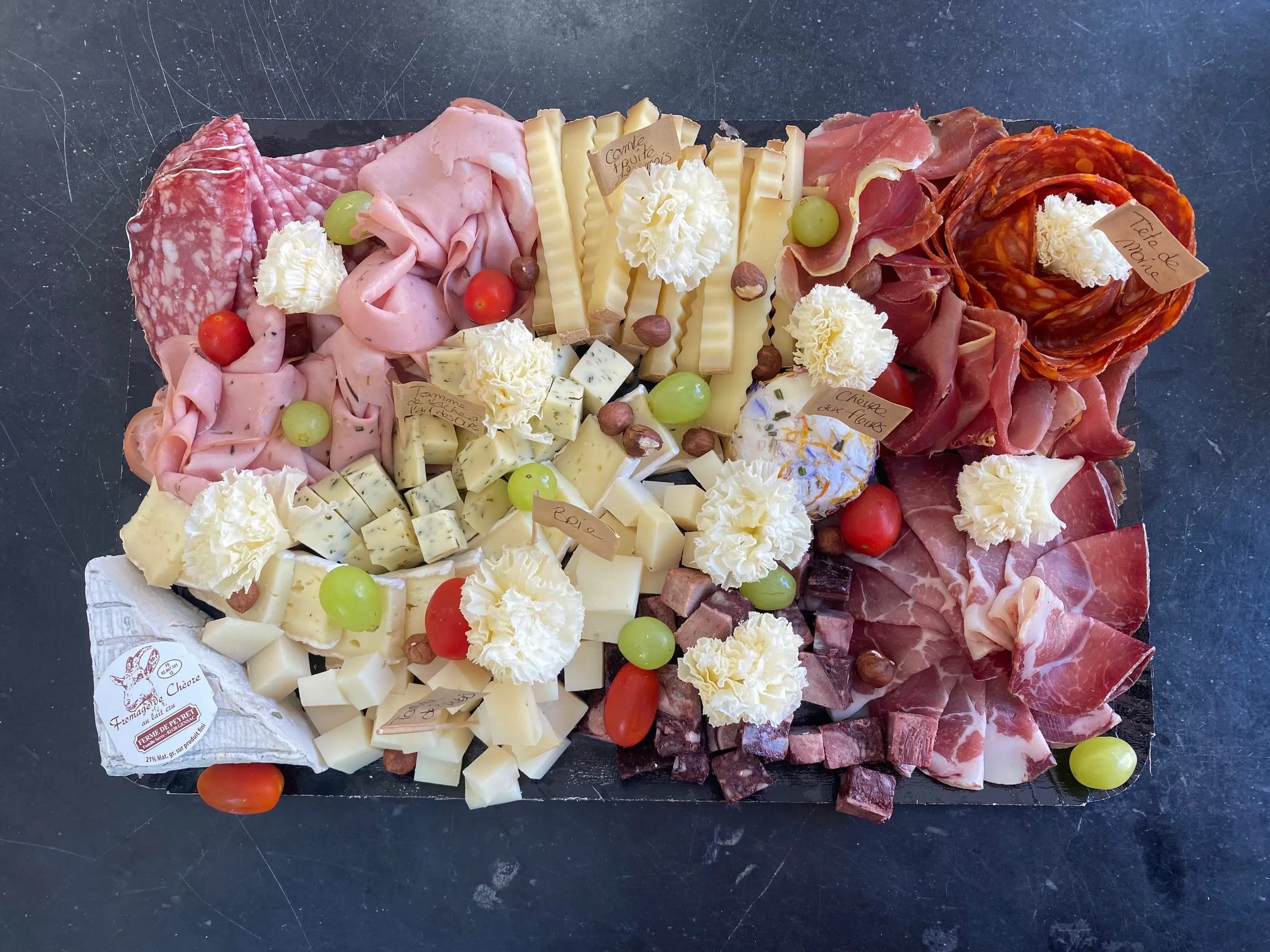 Plateau garni de charcuteries, de fromages, de raisins, de tomates et de noisettes