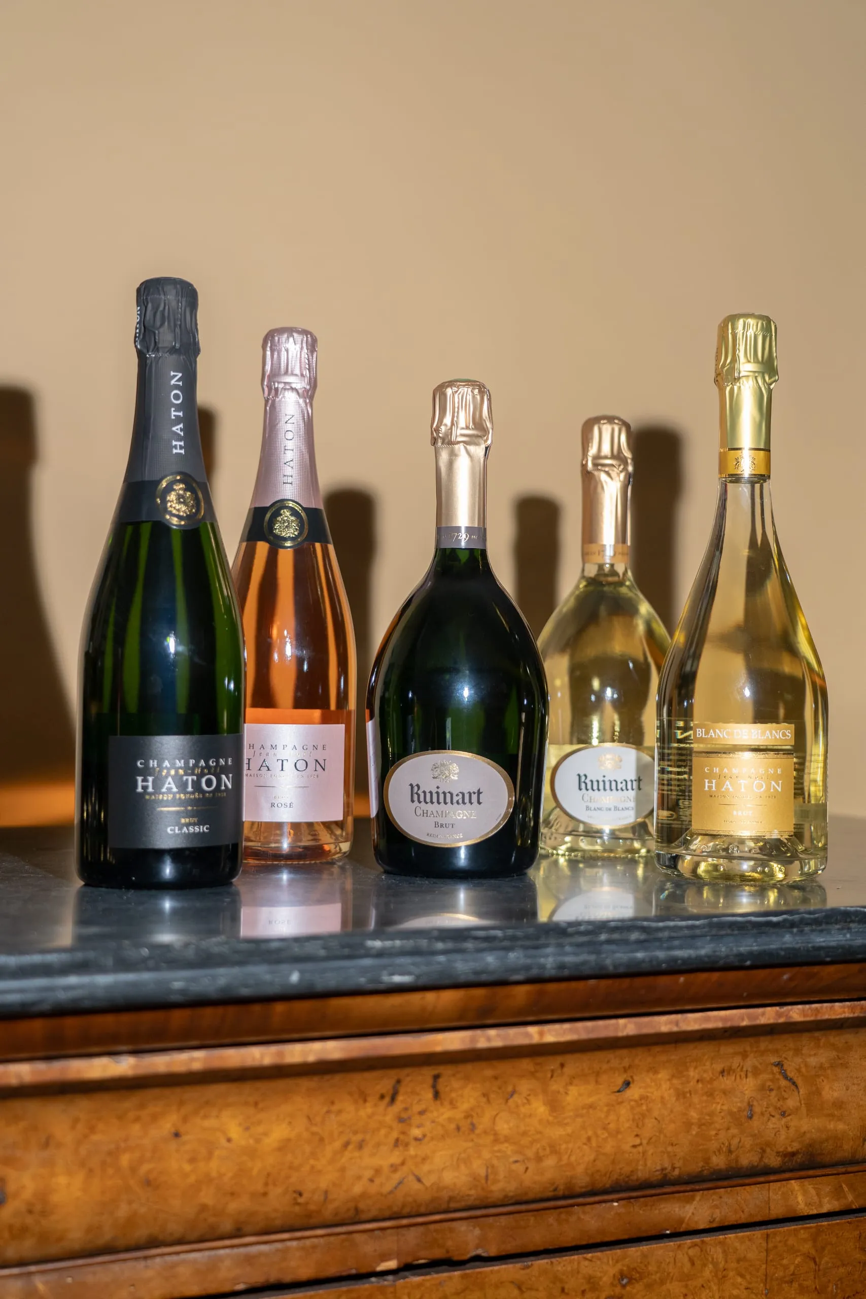 Cinq bouteilles de champagne brut, rosé et blanc de blancs alignées sur un comptoir